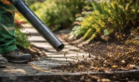 Landscaper using a leaf blower on a garden pathway